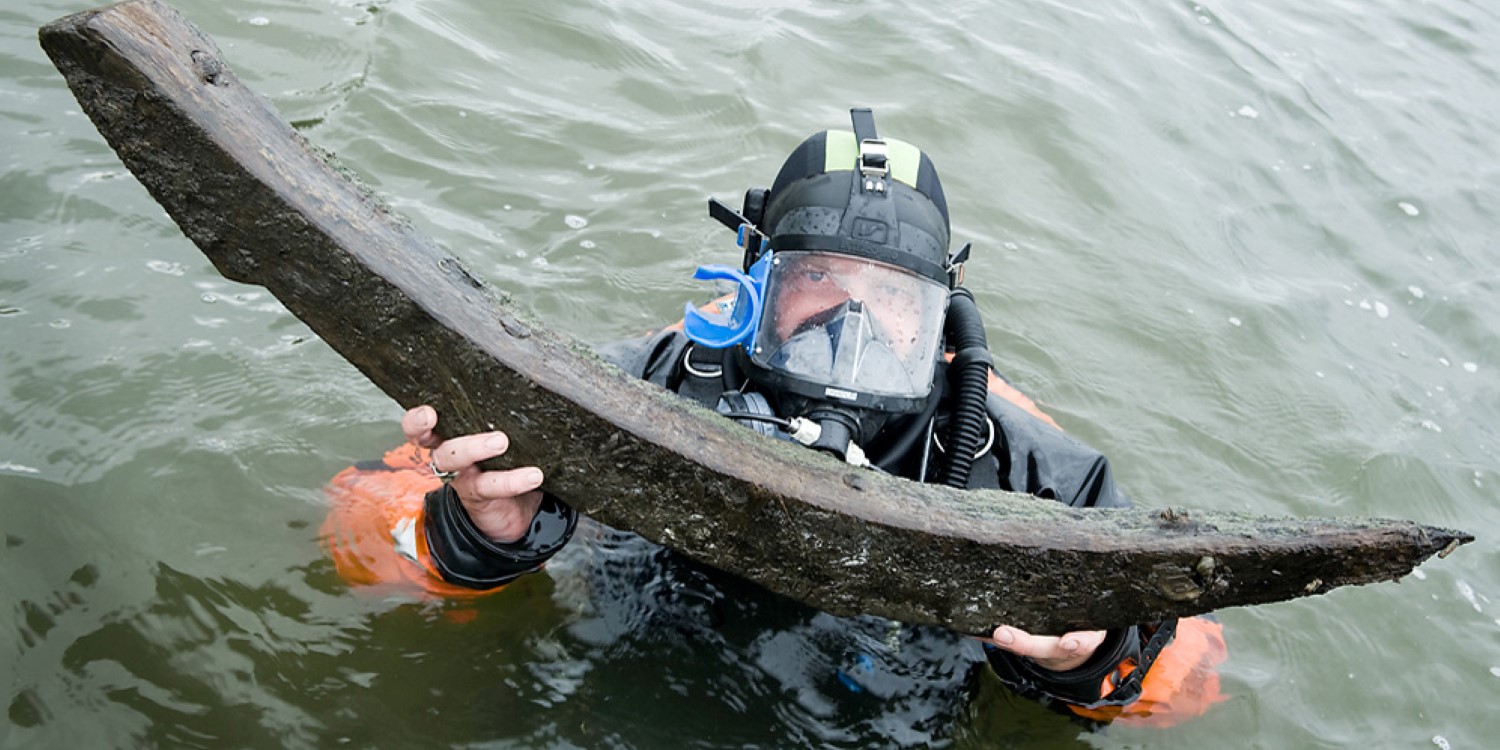 En dykare håller upp ett stort böjt föremål i järn. 