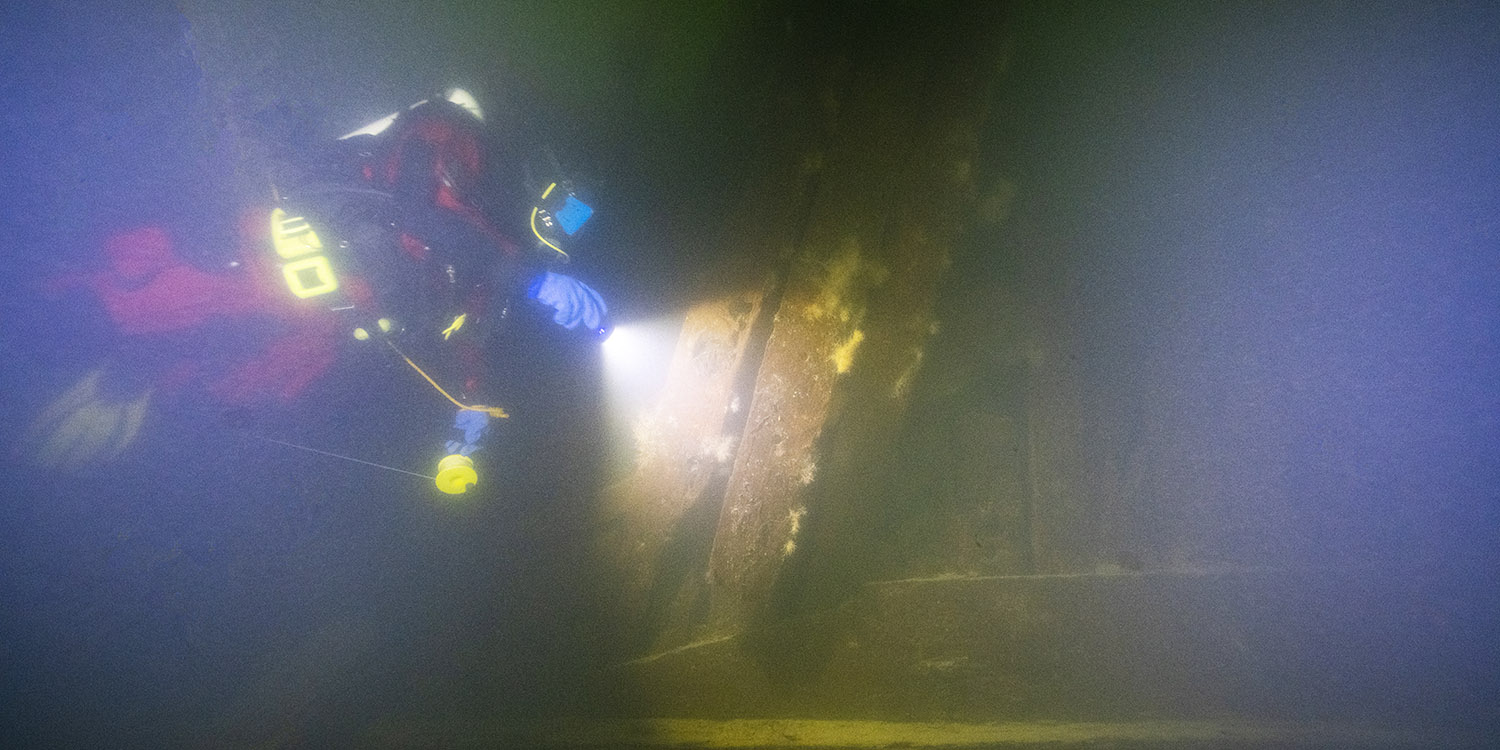 En dykare ses undersöka ett vrak på botten.