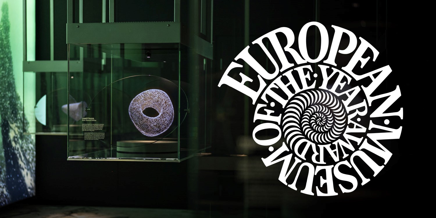 Glasmonter med ett ringformat föremål på piedestal. Till höger syns en vit cirkulär logotyp med spiralformad text mot mörk bakgrund