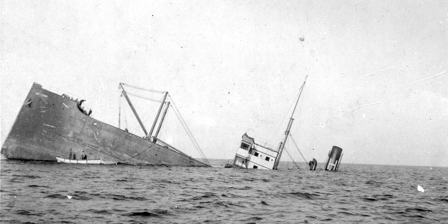 Svartvit fotografi av ett fartyg där dess för och överbyggnad sticker upp ur havet medan resten ligger under vattenytan.