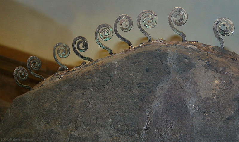 Närbild av en rundad sten eller metallisk yta med flera små spiralformade metallornament fästa längs ovankanten.