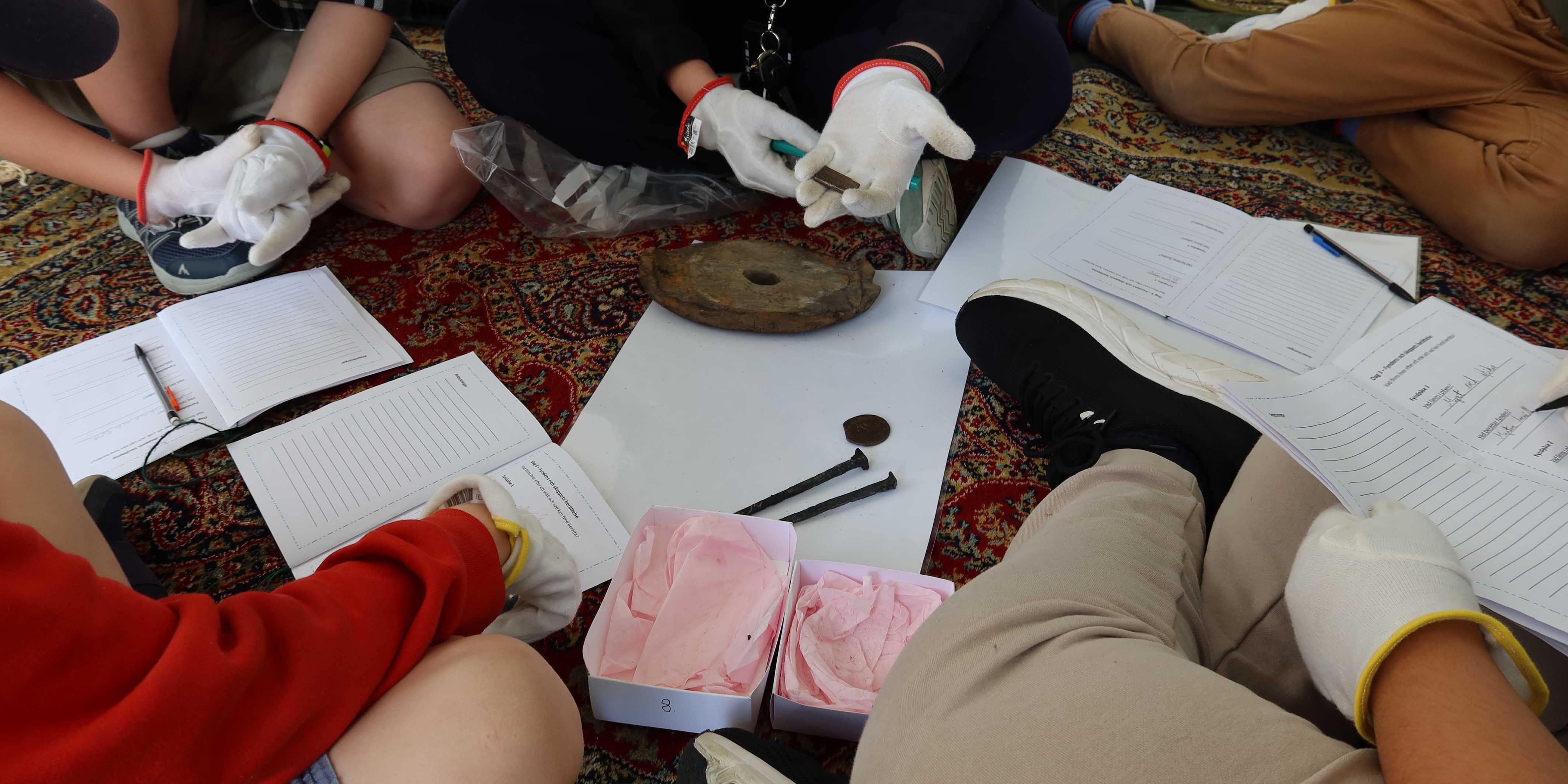 Barnhänder undersöker föremål i vita askar, bland annat spikar. 