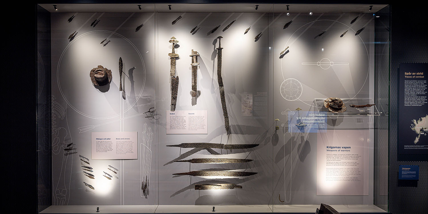 Monter med svärd, pilspetsar och andra vikingatida vapen upphängda mot ljus bakgrund.
