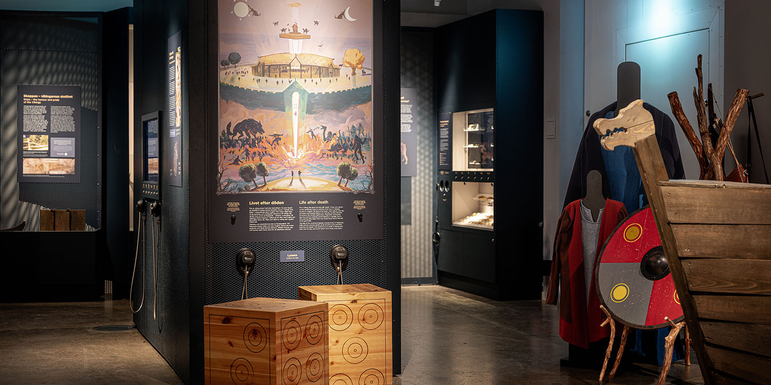 Utställningsrum med illustration av Valhall, montrar med föremål samt vikingakläder och sköld i förgrunden.