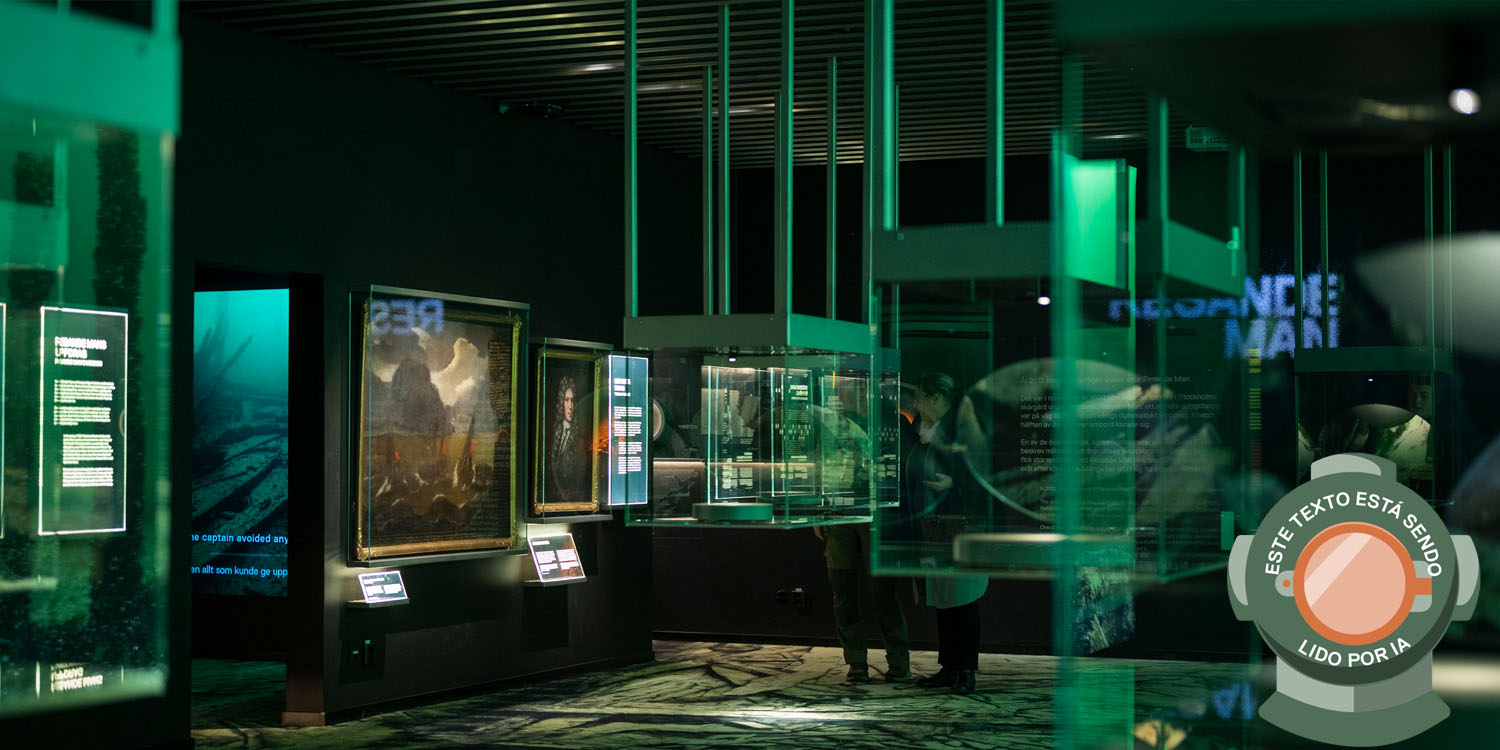 Utställningshall i museet Vrak gröntonat ljus och montrar med hologram syns, historiska målningar hänger på en vägg.  Bilden är märkt med en dykhjälm och texten: Este texto está sendo lido por IA.