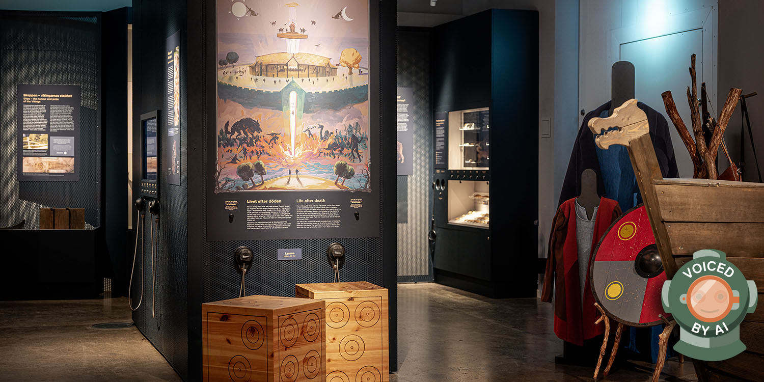 Utställningsrum med illustration av Valhall, montrar med föremål samt vikingakläder och sköld i förgrunden. Bilden är märkt med en dykhjälm och texten Voiced by AI.