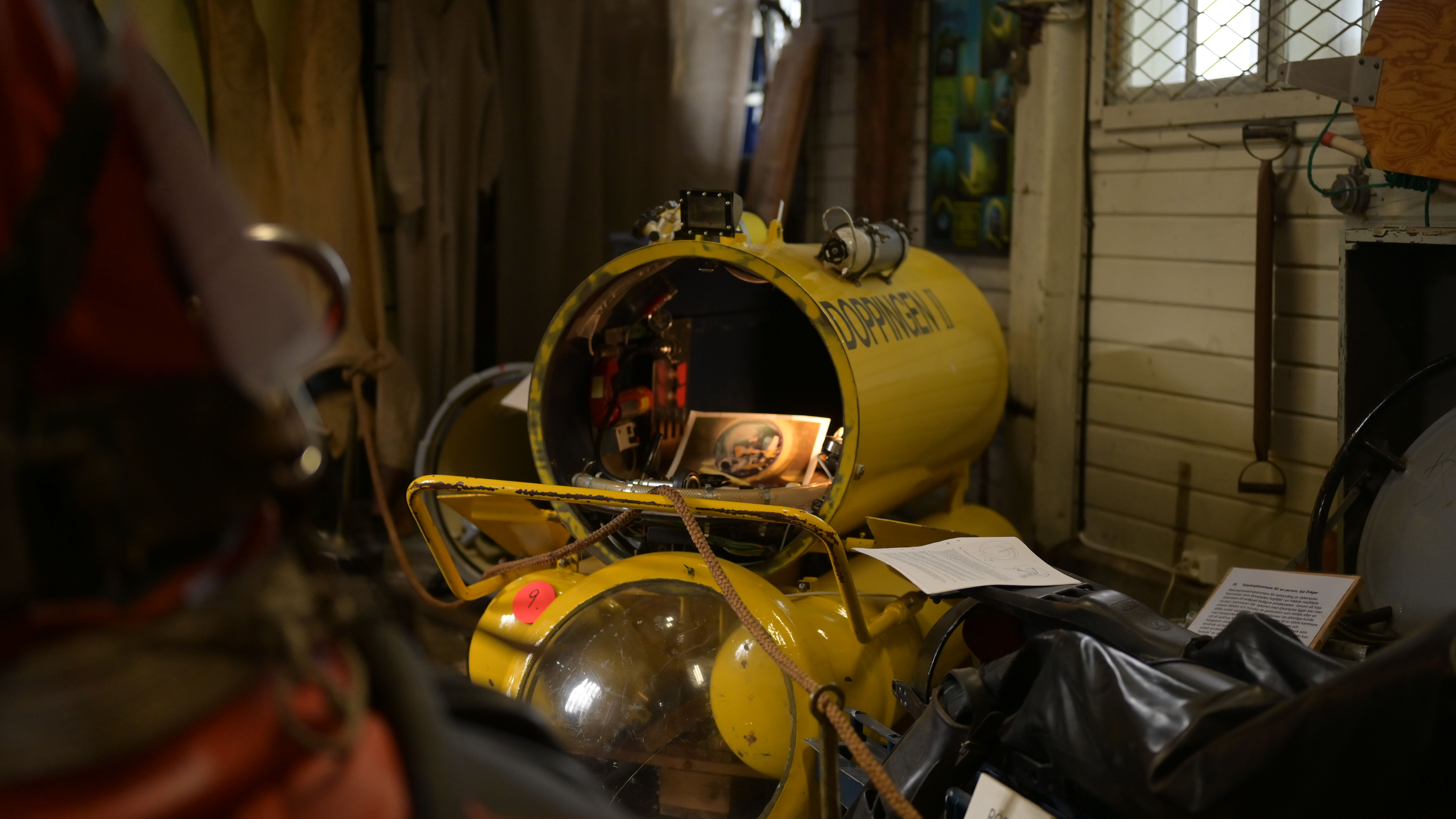 En gul miniubåt med öppen förarkapsel visas i ett museum, omgiven av dykutrustning och informationsskyltar