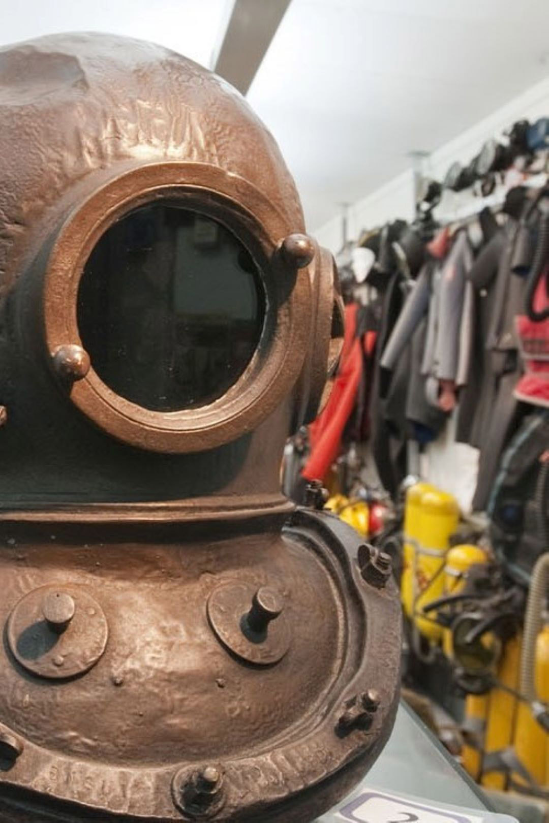 Dykarhjälm på gammaldags dykardräkt framför rader av kläder.