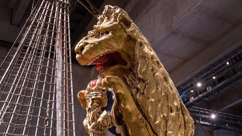 Förgylld skulptur av lejon syns framför skeppsrigg i Vasamuseet.