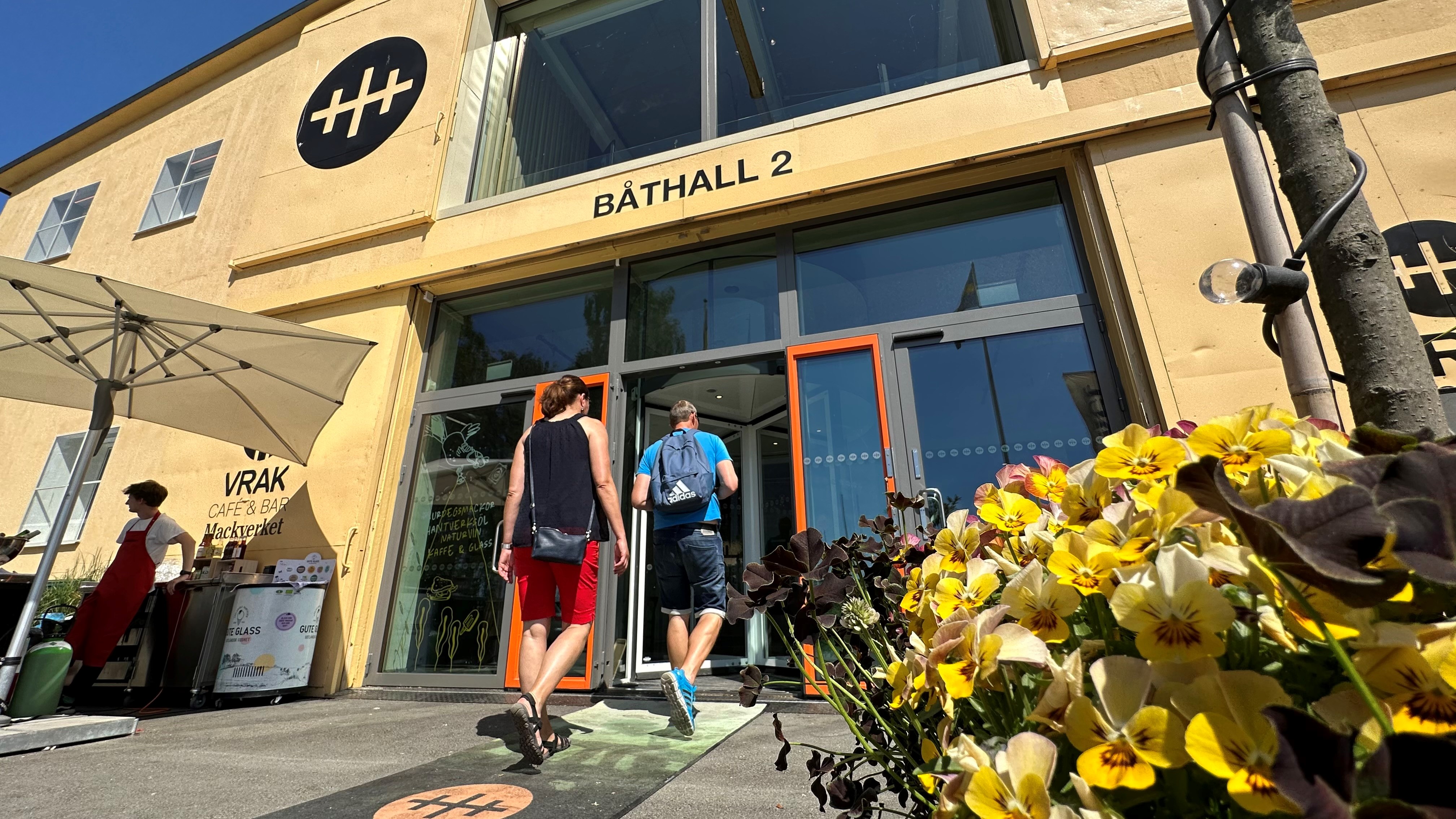 Besökare är på väg in i en ljusgul byggnad med logotypen av Vrak på fasaden.