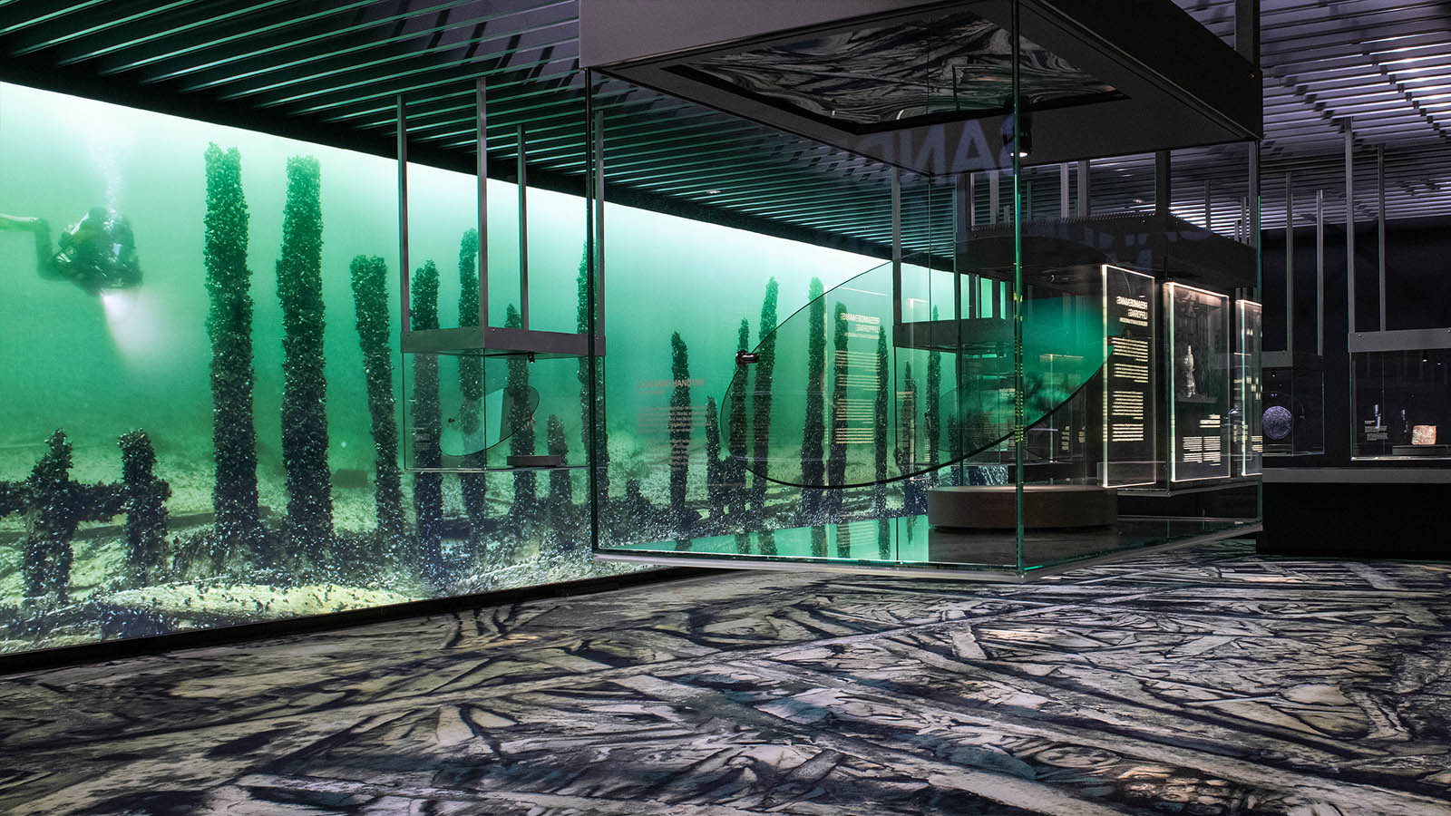 A room in a museum exhibition featuring paintings and glass cases suspended from the ceiling.