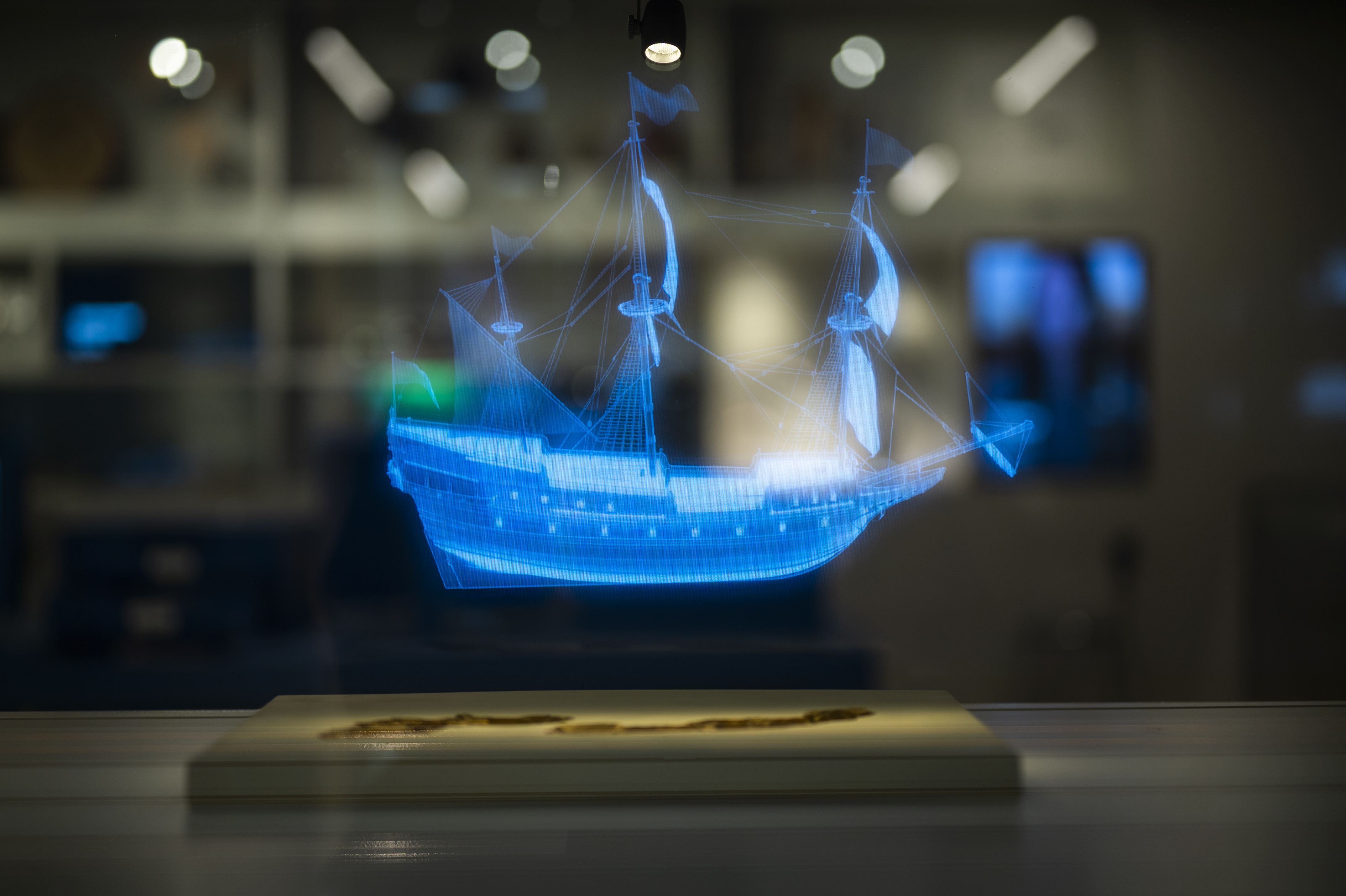 Ett blått hologram av ett historiskt segelfartyg visas ovanför en modell av ett skeppsvrak.