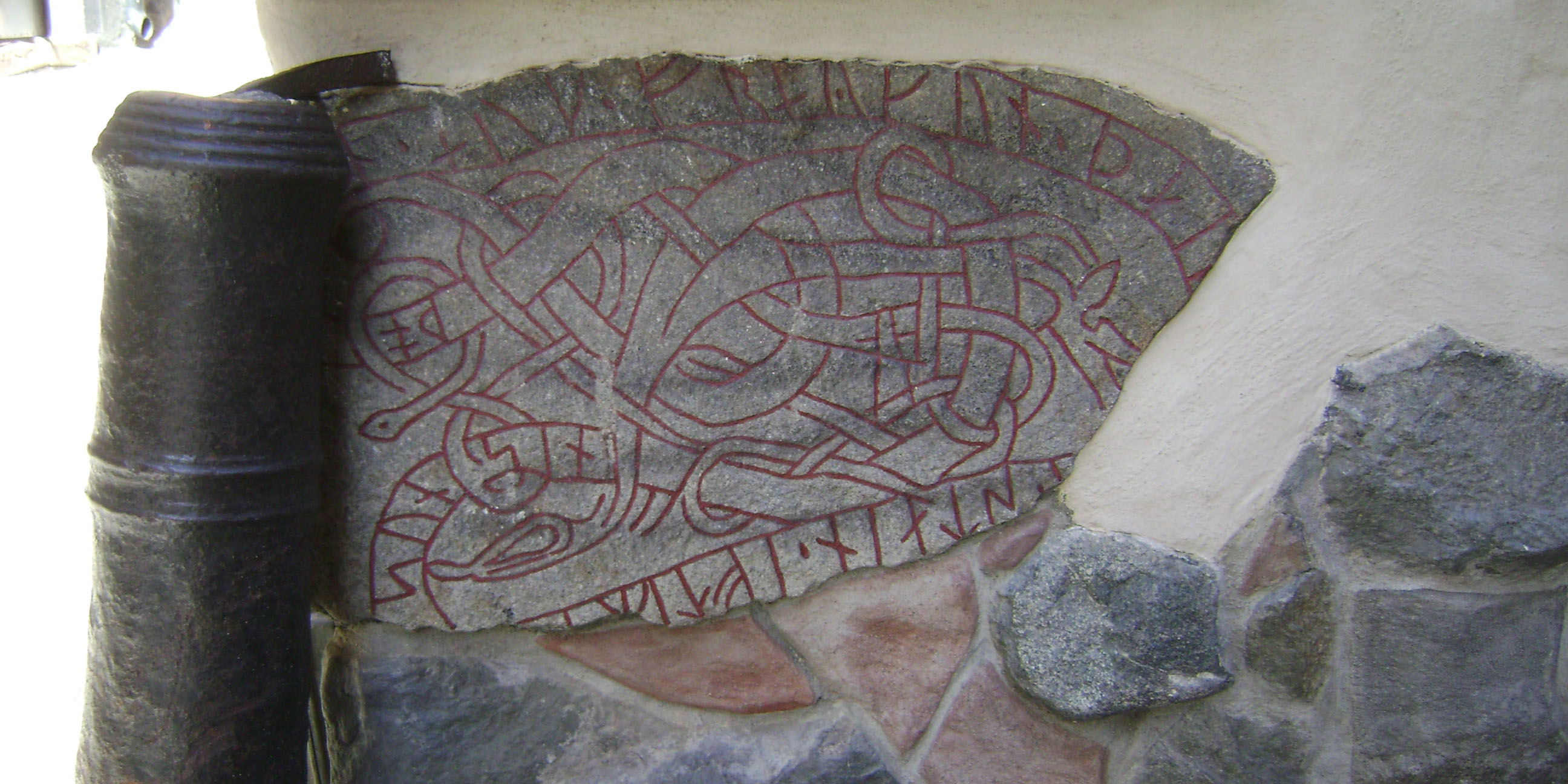 Liggande runsten imurad i vägg. 