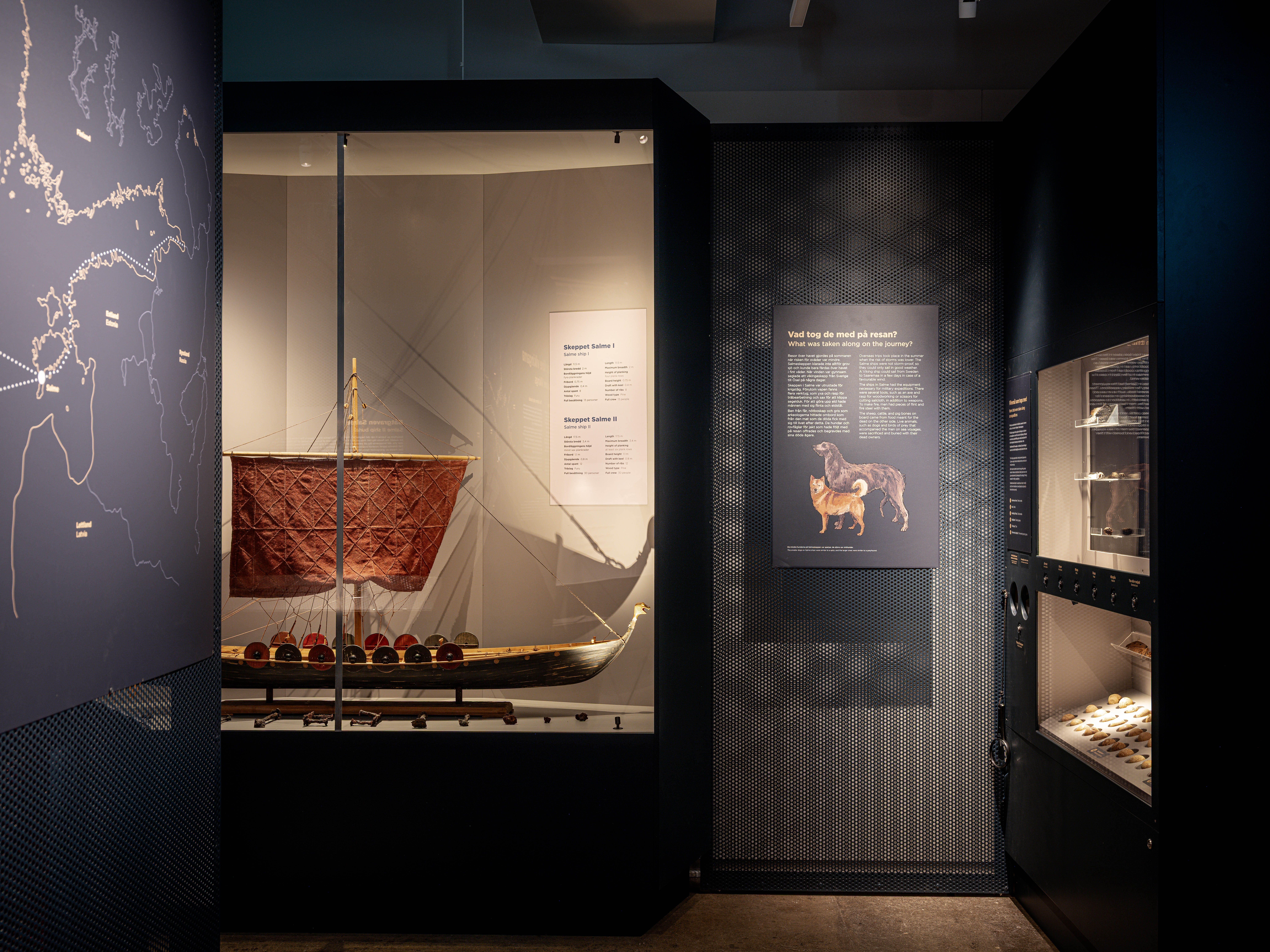 Utställningsdel med modell av ett vikingaskepp med rött segel och informationsskyltar på väggarna om resor och fynd.