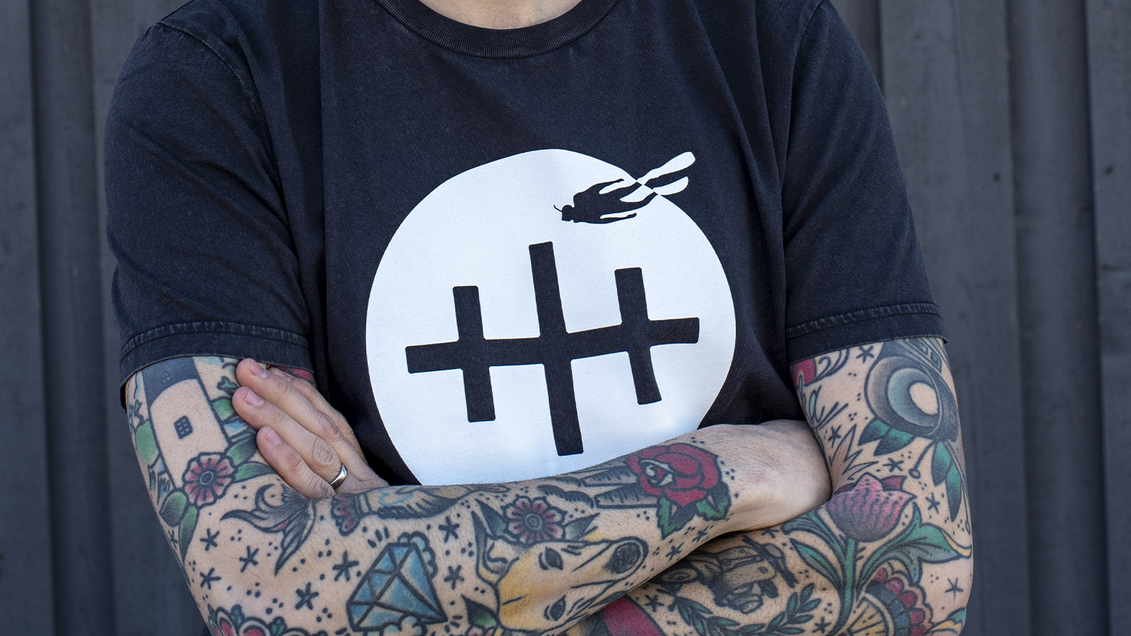 Vraklogga på t-shirts som bärs av person med tatueringar