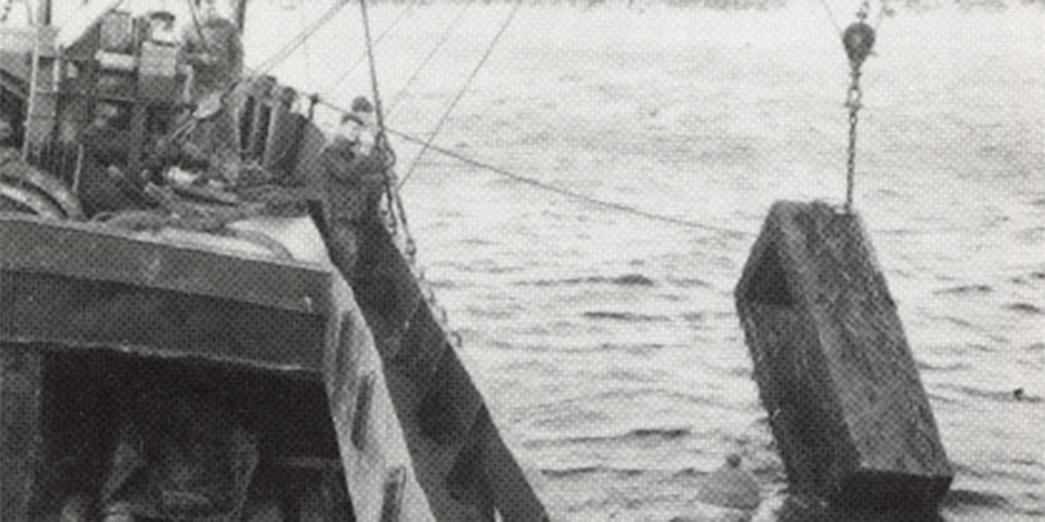 Svartvitt foto ur tidningsom visar hur en stor kista vincshas upp ur havet