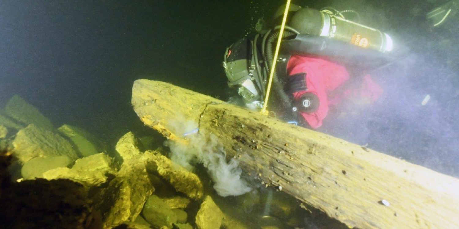 En person sågar igenom en tjock planka med tigersåg under vattenytan.