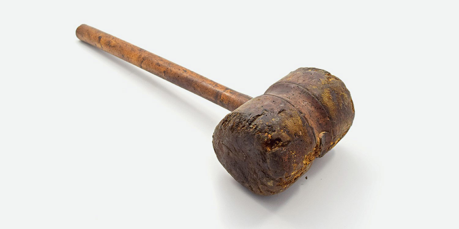 A wooden club with dents on a white back ground.