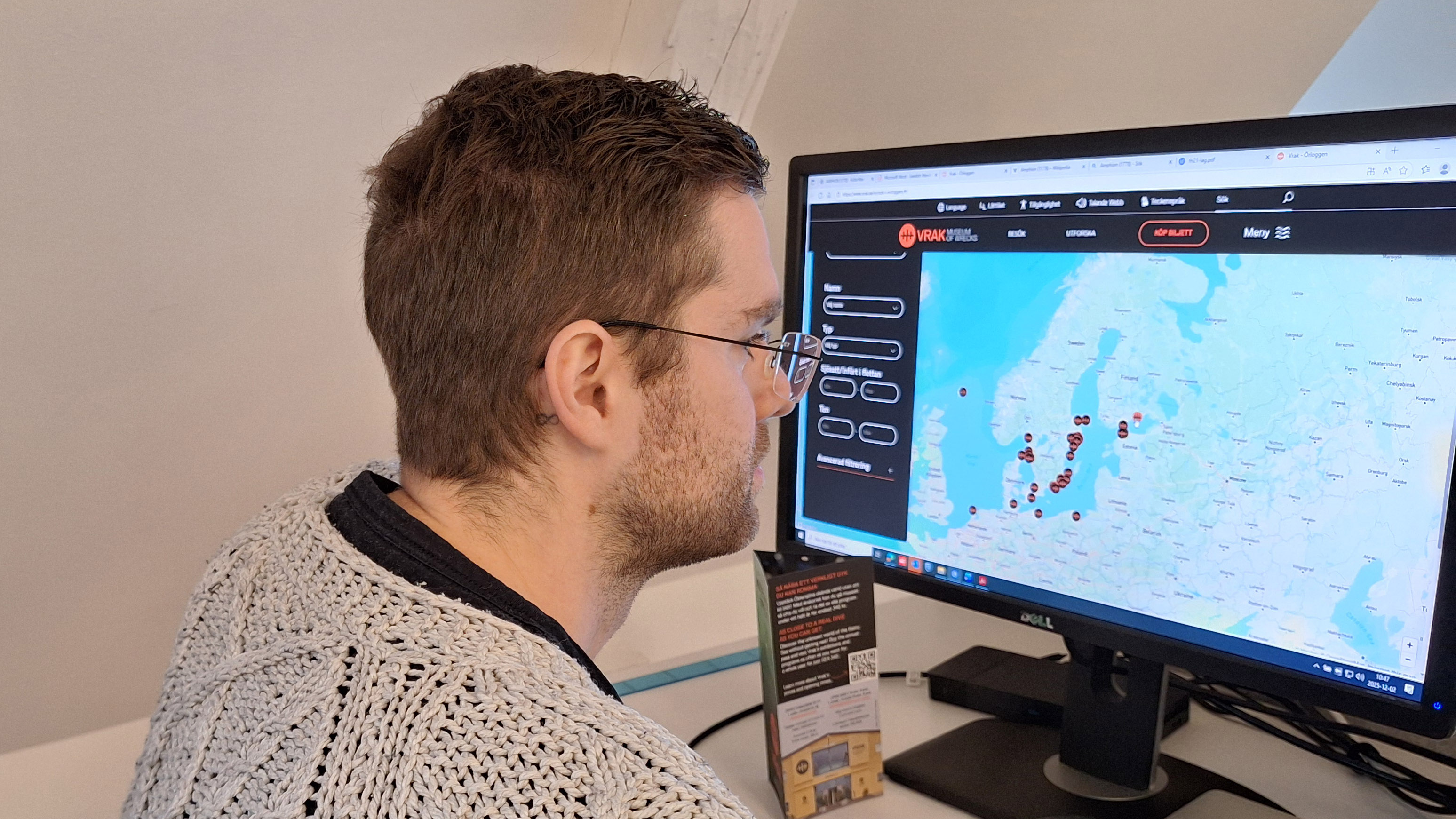 Man med kort hår och glasgon sitter framför en datorskärm där en karta över Östersjöområdet med runda markeringar syns. 
