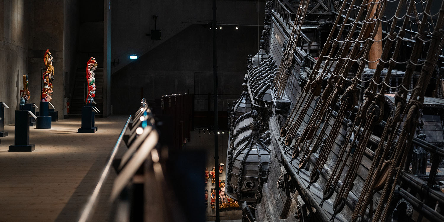 Foto av skeppet Vasa inne i museet, skeppets övre däck syns bredvid återskapade skulpturer från skeppet.