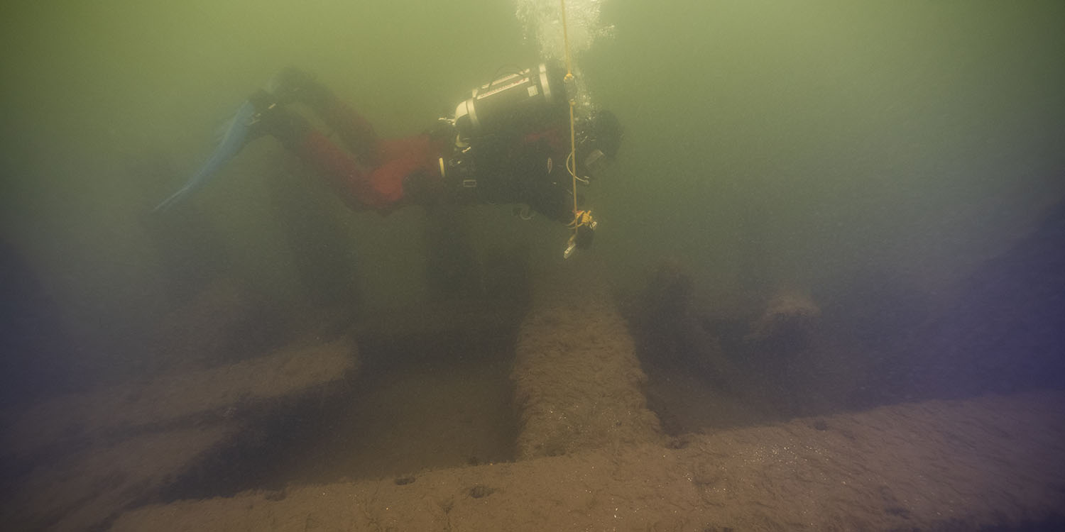 Undervattensfoto med dålig sikt av dykare i förgrunden och vrak i bakgrunden