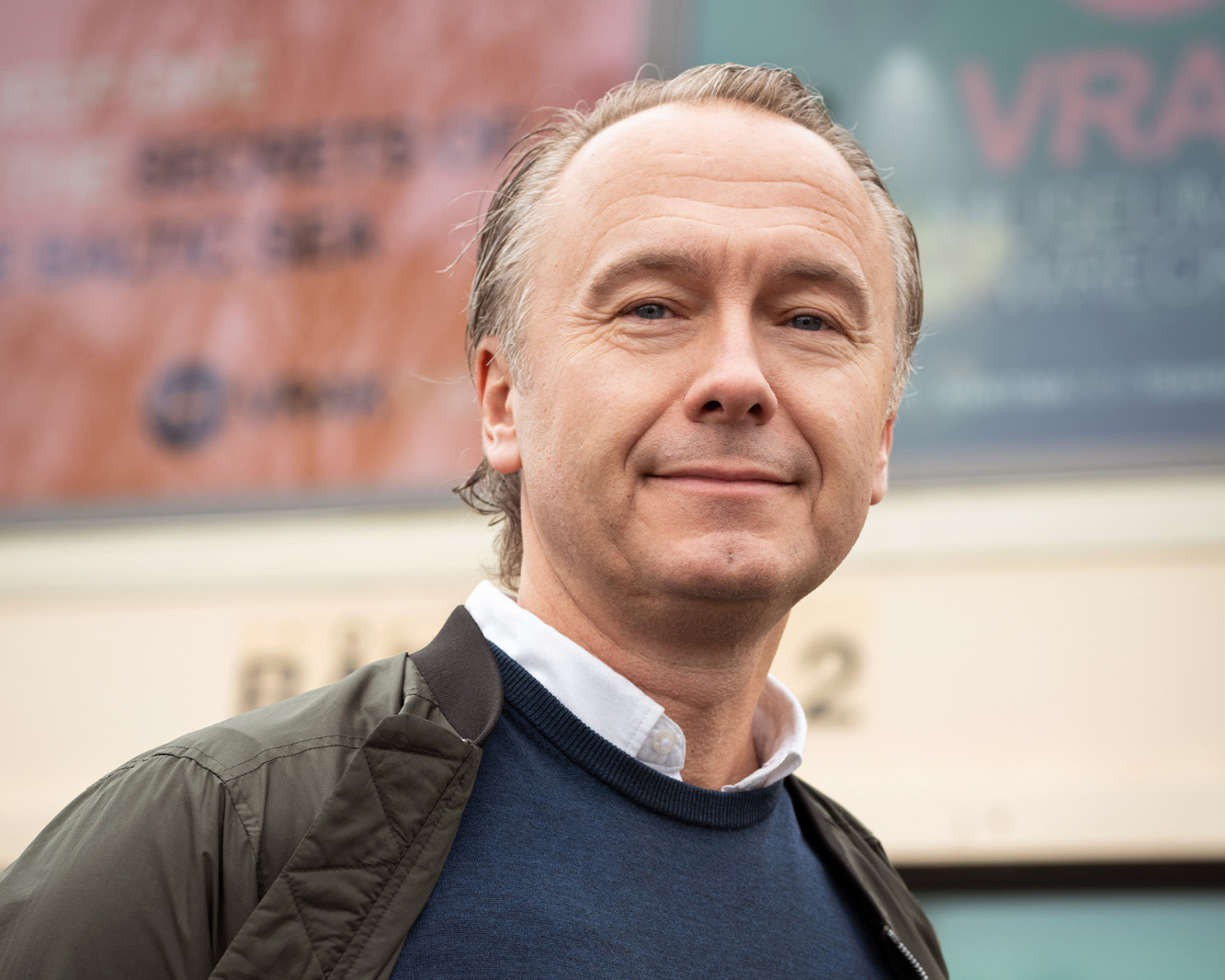 Foto av leende medelålders man i grön jacka och blå tröja. 