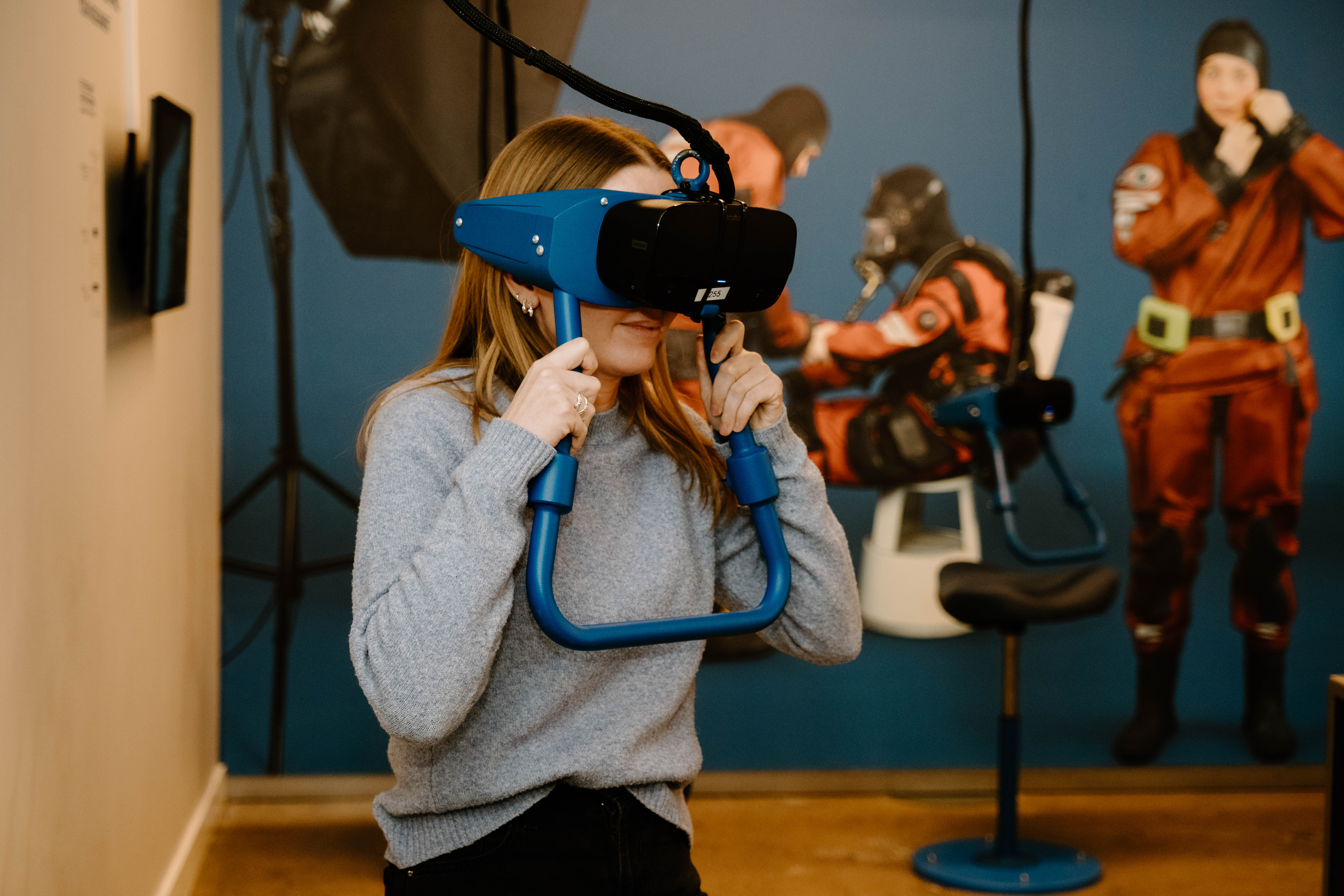 Woman trying on a virtual reality headset in front of photo wall with divres.
