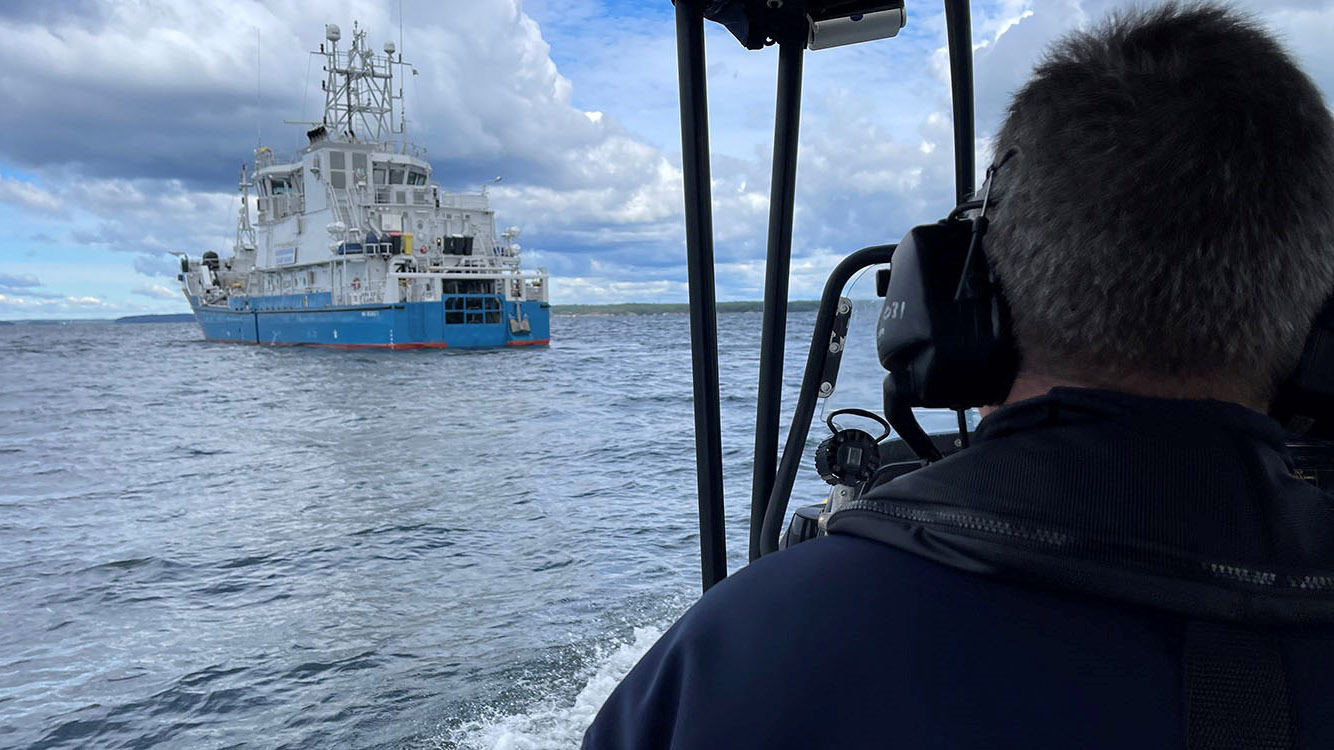 Foto av fartyg från kustbevakningen med gråhårig persons bakhuvud i förgrunden. 