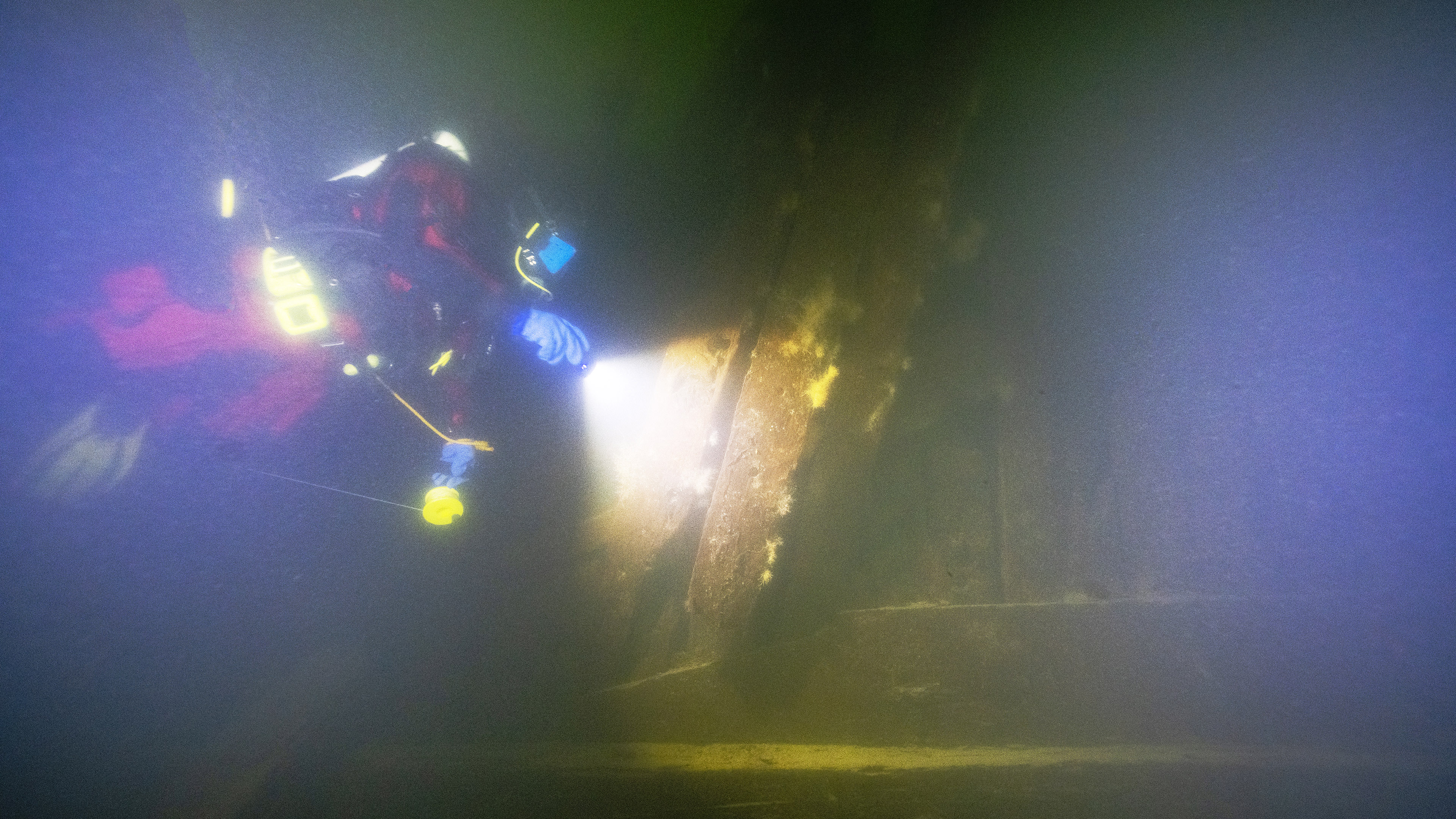 Diver under water shines a light on side of ship with gun port.