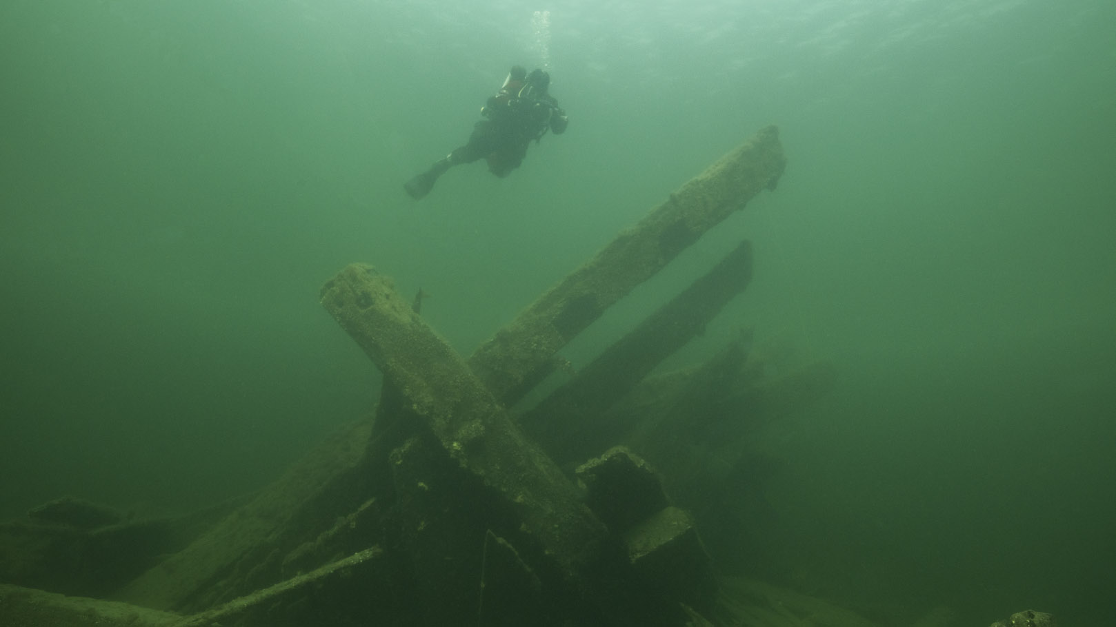 Green tinted underwater photo of diver above wreck of Swedish ship Enigheten. 