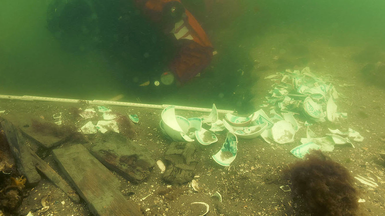 Dykare i rött ovanför porslinskärvor på vraket efter ostindiefararen Götehborg.
