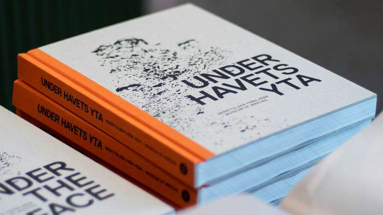 Foto av böcker med orange rygg och grå framsida på ett bord.