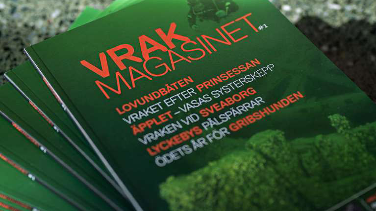 Flera exemplar av en tidskrift med omslag i grönt och orange ligger på ett bord i solfjäderform.