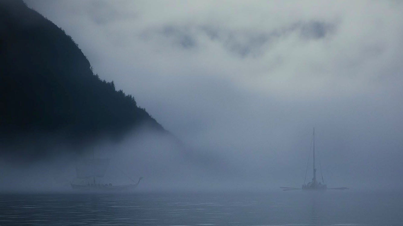 Dimmig vik där vikingaskepp syns på vatten. 